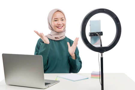 Asian Muslim woman with laptop and mobile phones with lighting equipment make a vlog isolated over...