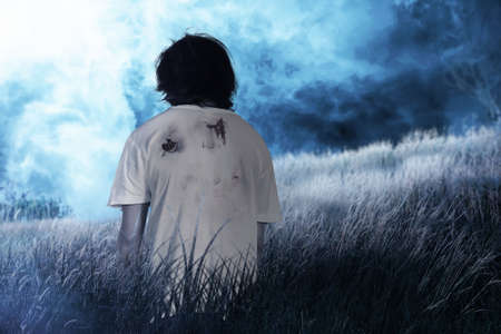 Scary zombie with blood and wound on his body walking on the field