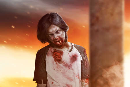 Scary zombie with blood and wound on his body standing with dramatic backgroundの写真素材