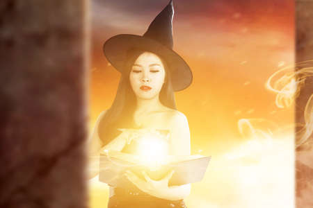Asian witch woman with spellbook showing magic on her hand with dramatic backgroundの写真素材