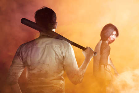 Asian man standing with a baseball bat in his hand ready to attack zombies with dramatic backgroundの写真素材