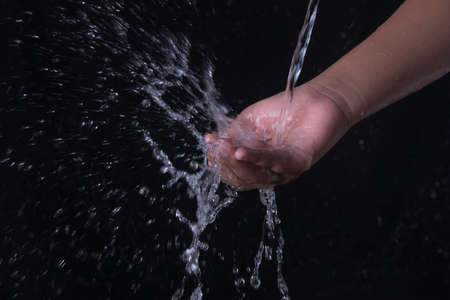 Pouring water splashing on hand with black backgroundの写真素材