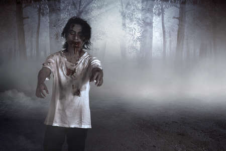 Scary zombie with blood and wound on his body walking on the forestの写真素材