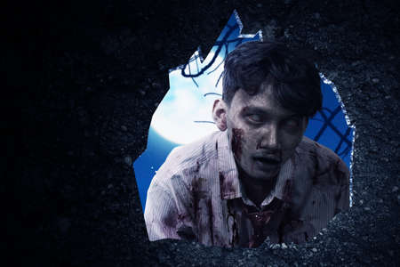 Wall hole with a scary zombie standing with night scene backgroundの写真素材