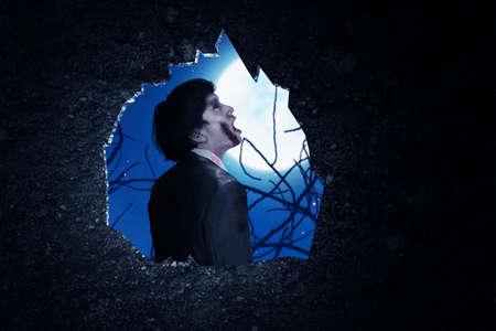 Wall hole with a scary zombie standing with night scene backgroundの写真素材