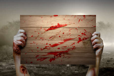 Zombie hand with blood and wound holding a wooden signboard with the dramatic scene backgroundの写真素材