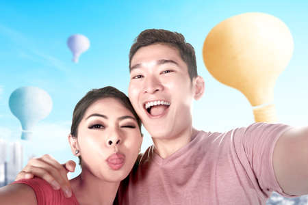 Asian couple taking a selfie with colorful air balloon flying with cityscape background