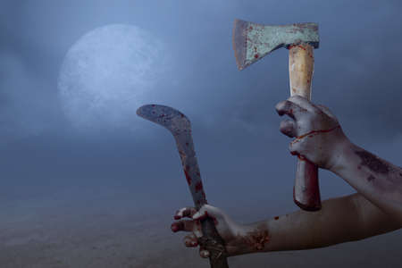 Zombie hands with wound holding ax and sickle with the night scene backgroundの写真素材