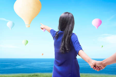 Asian woman pointing colorful air balloon flying with blue sky backgroundの写真素材