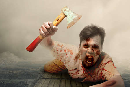 Scary zombie with blood and wound on his body holding ax crawling with foggy backgroundの写真素材