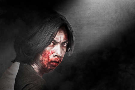 Scary zombie with blood and wound on his body standing with dark background