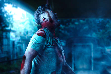 Scary zombie with blood and wound on his body walking on the cemetery