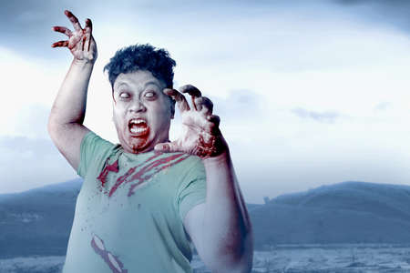 Scary zombie with blood and wound on his body walking on the fieldの写真素材