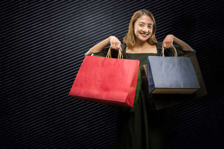 Asian woman carrying a shopping bag with a black background. Black Friday conceptの写真素材