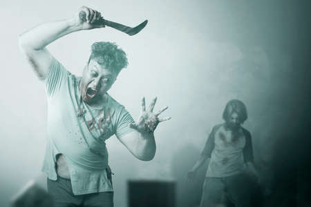Scary zombie with blood and wound on his body holding sickle walking on the cemetery