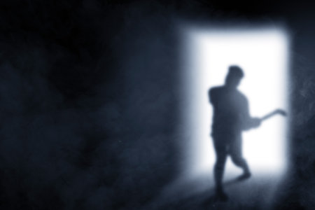 Silhouette of scary zombie with blood and wound on his body holding sickle coming from bright door backgroundの写真素材
