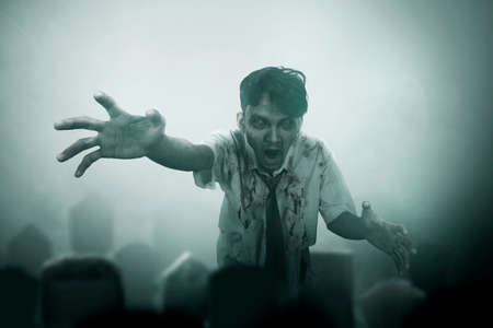 Scary zombie with blood and wound on his body walking on the cemetery