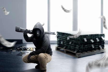 Criminal man in a hidden mask sitting and holding the shotgun while robbery the money on the bank