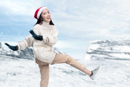Asian woman with winter gloves and Santa hat standing on the snowfield