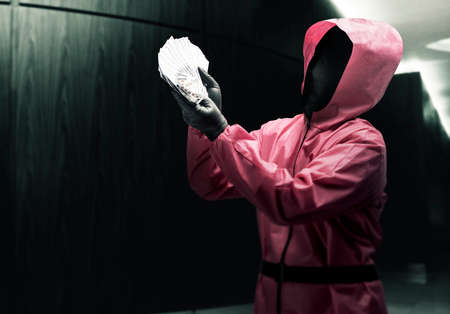Criminal man in pink uniform and a hidden mask holding the money after the robbery the house