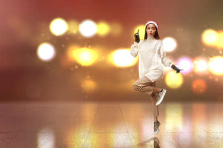 Asian woman with winter gloves and Santa hat standing on with blurred light background