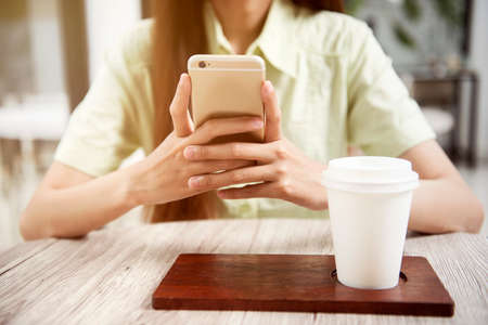 Woman with coffee on the table using a mobile phone in the coffee shopの写真素材