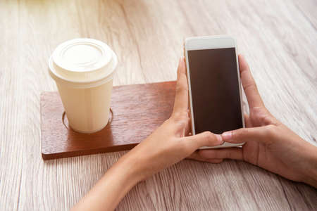 Woman with coffee on the table using a mobile phone in the coffee shop. Empty screen for copy spaceの写真素材