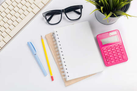 Computer keyboard and note book with pen and pencil on white deskの写真素材