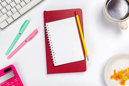 Computer keyboard and note book with pen and pencil on white deskの写真素材