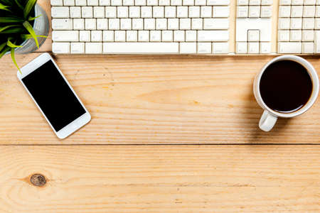 Computer keyboard with mobile phone and cup of coffee on wooden deskの写真素材