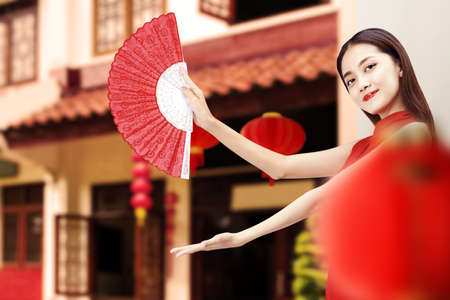 Asian Chinese woman in a cheongsam dress holding fan with open palm showing something. Happy Chinese New Yearの写真素材