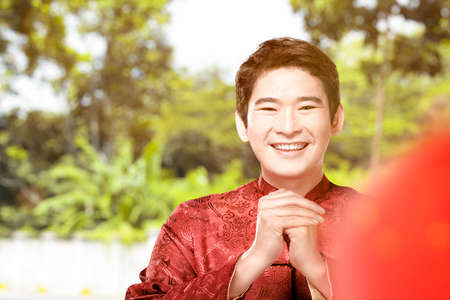 An Asian Chinese man in a cheongsam dress with a congratulations gesture. Happy Chinese New Yearの写真素材