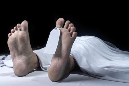 Human corpse covered with a sheet and name tag on toe in the morgue