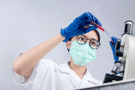 Asian researcher woman with face mask and glasses holding medical tube on the labの写真素材