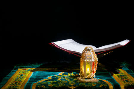Quran open on a wooden placemat in prayer rug with prayer beads and Arabic lamp on dark backgroundの写真素材