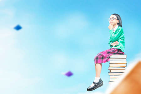 Asian little girl with eyeglasses sitting on the stack of books. World Book Day