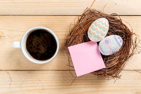 Colorful easter egg on the nest with empty notepaper and cup of coffee on a wooden table. Happy...
