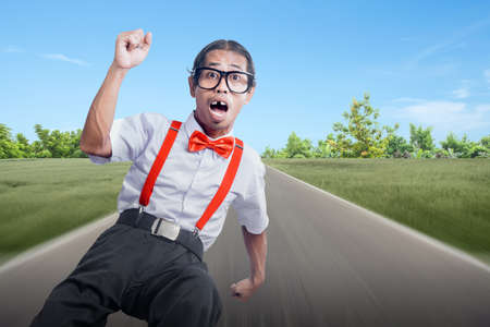 Asian nerd with ugly face running on the street with blue sky backgroundの写真素材