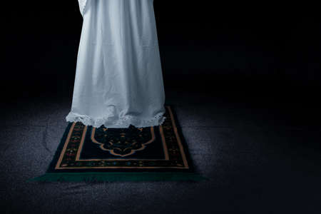 Muslim woman in veil in praying position (salat) on the prayer rug with dark background