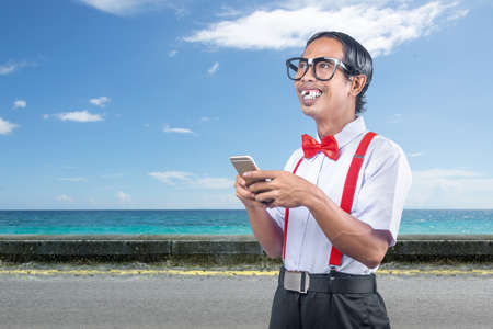 Asian nerd with an ugly face holding mobile phone on the street