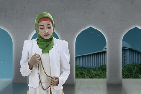 Asian Muslim woman in veil praying with prayer beads on her hands on the mosqueの写真素材