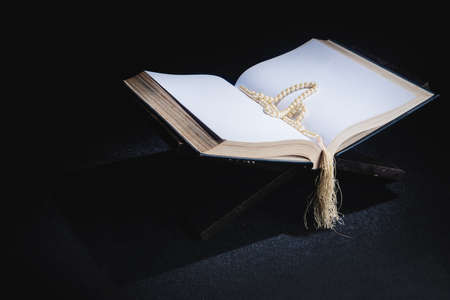 Quran open on a wooden placemat with prayer beads on the dark background
