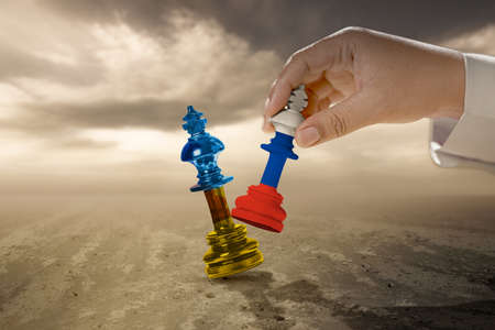 Human hand holding chess piece king with Russian flag to beat chess piece king with Ukraine flag...