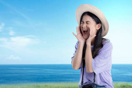 Asian woman with hat and camera yelling something with blue sky backgroundの写真素材