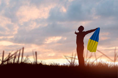 Silhouette of a businessman holding Ukraine flag with sunrise backgroundの写真素材