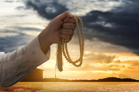 Muslim man praying with prayer beads in his hands with the dramatic scene backgroundの写真素材