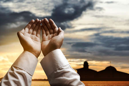 Muslim man standing while raised hands and praying with the dramatic scene backgroundの写真素材