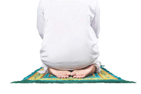 Close up view of a Muslim man in a praying position (salat) on a prayer rug isolated over white backgroundの写真素材