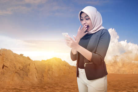 Asian Muslim woman in a headscarf holding a mobile phone with blue sky background