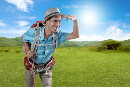 Asian man with a hat and backpack is looking at something on the field with blue sky background